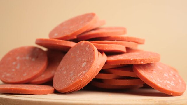 Pile of pepperoni slices in close up motion on wooden board.