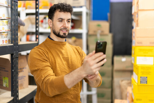 Young worker uses smartphone to scan boxes in grocery warehouse