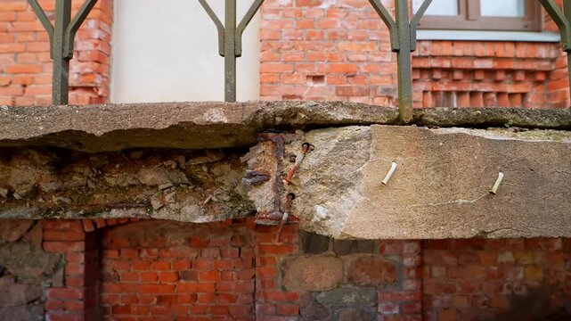 Close-up of crumbling balcony slab with exposed rebar and patchy cement repair above a brick wall, showing poor workmanship, corrosion, and structural deterioration.