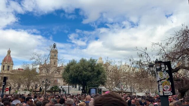 Large crowd of people waiting for Mascleta at Plaza del Ayuntamiento, Valencia, experiencing the traditional Fallas festival with historic buildings and blue sky as a backdrop