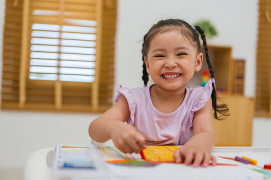 happy preschool child girl drawing and painting with colorful oil pastels on paper