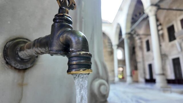 Ornate antique bronze faucet outdoors water flowing on marble wall courtyard background.