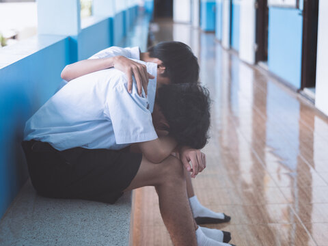 Supportive Friend Comforting Sad Student Sitting on School Hallway Floor