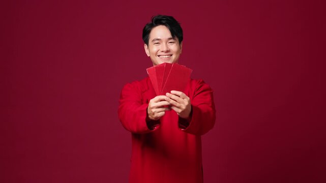 An Asian man holds red envelopes, joyful and makes gestures showing off the money. The video captures the festive atmosphere