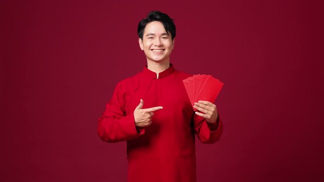 Asian man pointing while holding red envelope, confident and cheerful New Year pose. Copy space
