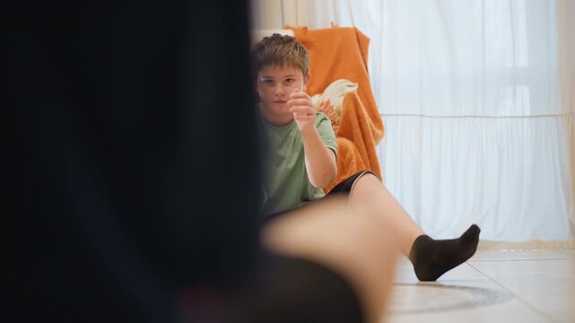 Caucasian teen at home kitchen waiting with melon on lap, expectant expression as figure approaches from foreground subtle interaction and gentle offer suggest teaching moment and family guidance