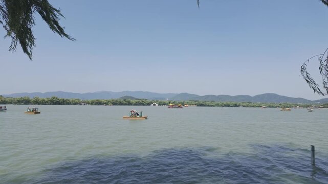 Scenic view of traditional Chinese dragon boats and pedal boats on Kunming Lake with mountains in the background at the historic Summer Palace in Beijing. Ideal for travel and cultural documentaries.