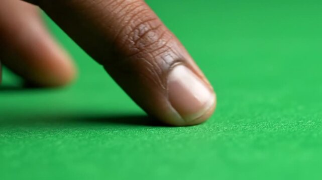 Close-up of a person's dark-skinned finger gently touching a vibrant green felt surface.