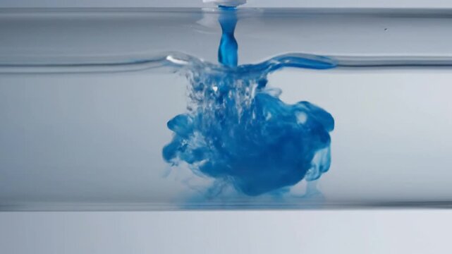 Blue ink drop dissolving in clear liquid inside a glass tube, abstract science experiment
