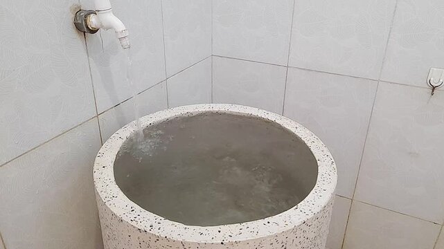 Tap water flowing into a white terrazzo bathtub. The tub is full to the point of overflowing.