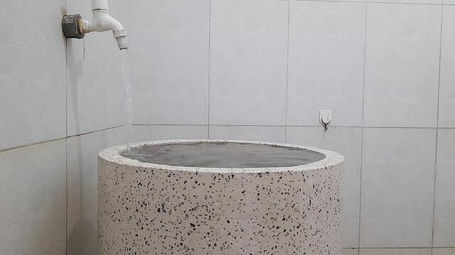 Tap water flowing into a white terrazzo bathtub. The tub is full to the point of overflowing.