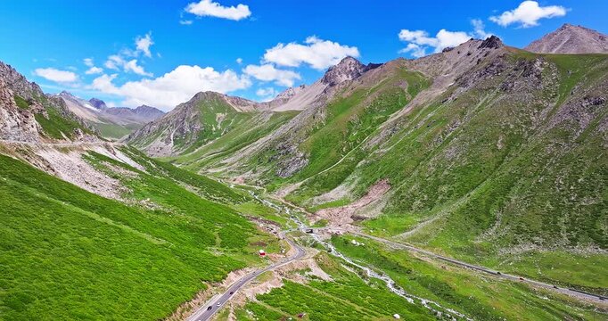 Aerial view of a winding road through a rugged high-mountain valley under a clear blue sky, Xinjiang, China.