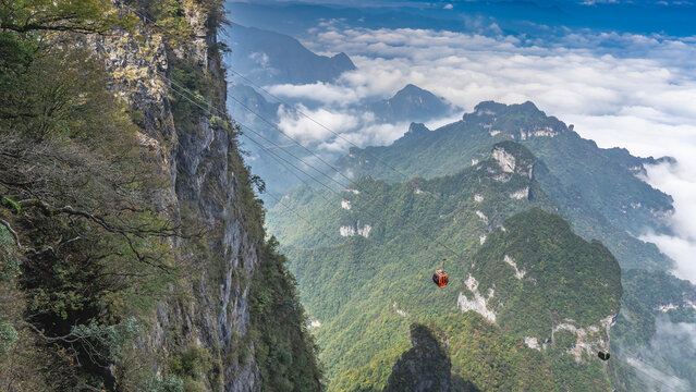 High-altitude cable car. A cabin funicular over a precipice. A sheer cliff face in the foreground. The peaks of beautiful mountains in white clouds. The blue sky. China. Zhangjiajie