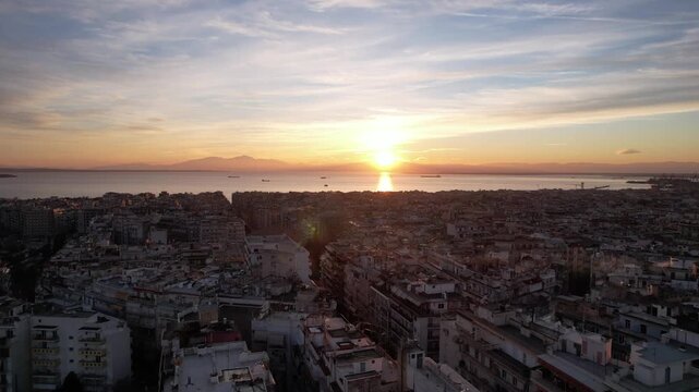 Aerial view flying backwards over thessaloniki city with the arch of galerius and the sea at sunset