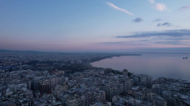 Aerial drone shot of thessaloniki cityscape and thermaic gulf with cargo ships at twilight
