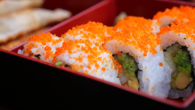 Fresh california sushi rolls with orange masago and avocado arranged in red lacquer bento.
