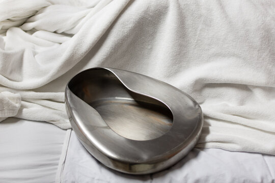 Stainless steel bedpan on white hospital bed with soft fabric highlighting medical care hygiene patient support and clinical environment with copy space