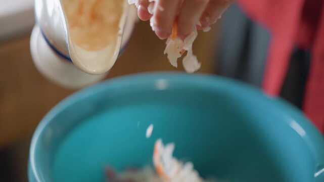 Hands draining shredded cabbage over bowl, home cook gently squeezing ceramic colander into blue basin with minced pork, closeup of dripping liquid and careful fingers, calm morning kitchen prep.