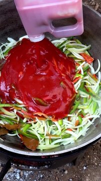 Pouring tomato sauce on freshly cut vegetables cooking outdoors