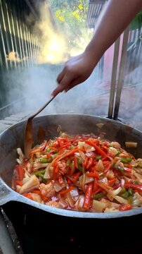 Chef stirring a large cauldron of steaming vegetable stew outdoors