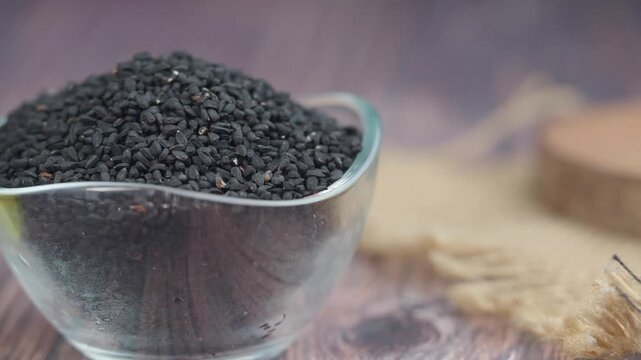 Close up of black cumin seeds in glass bowl with oil bottle cinematic motion.