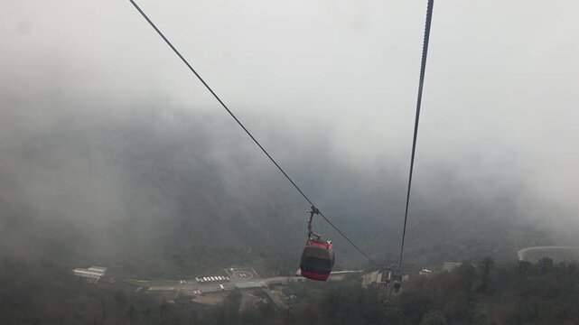 Wide Angle Shot of Red Gondola Lift (Cable Car) Descending Over Foggy Mountain Valley.