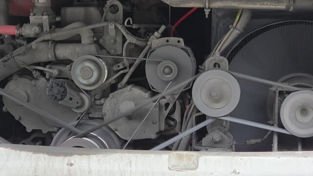 Close-up of a bus's dusty diesel engine with belts, pulleys, and cooling fan.