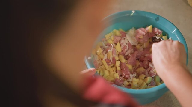 Salad preparation scene. Hands carefully mixing creamy salad with ham and potatoes in bright kitchen. Closeup of hands folding mayonnaise into potato and ham mixture during busy dinner preparation