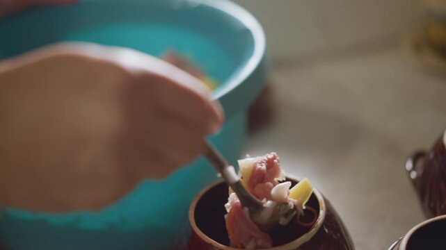 Preparing clay pot with minced mixture. Hands portioning seasoned mixture into ceramic vessel. Preparation scene of hands filling clay pot with seasoned minced ingredients from mixing bowl
