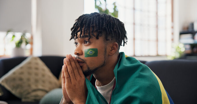 Man, sports and watching tv on couch with Brazil flag, concern and suspense for football competition. Black person, stress or nervous in home with anxiety, tension and broadcast for soccer world cup.