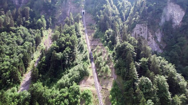 Aerial 4k drone view of the Stoos funicular climbing a steep forested mountainside, showcasing Swiss engineering, alpine transport, and scenic travel access to the Stoos mountain village