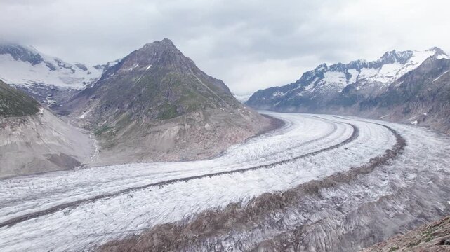 A cinematic aerial glide over the vast Aletsch Glacier, showcasing its signature curving path and dark medial moraines as it flows through a dramatic valley of rugged, snow-dusted Swiss mountain peaks