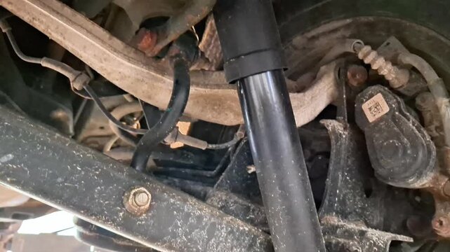 Close up view of vehicle suspension showing shock absorber, control arm, and wheel assembly, highlighting mechanical parts, bolts, and brackets in a workshop repair setting