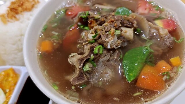 Traditional Indonesian oxtail soup sop buntut with vegetables and rice