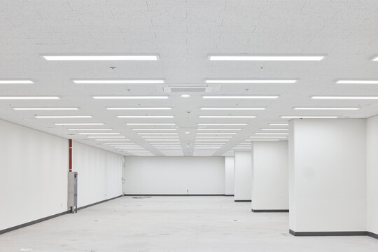 Large empty white commercial room with central columns and bright ceiling grid