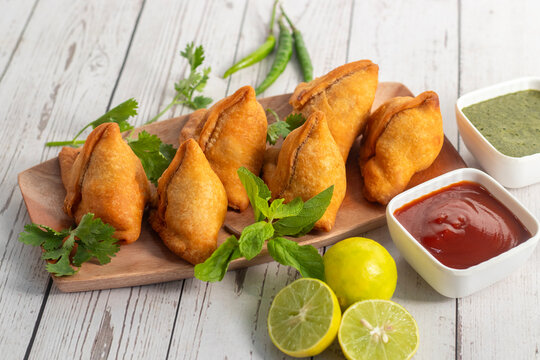 Crispy golden samosa served with mint chutney tomato sauce fresh lemon on wooden board Indian street food snack delicious appetizer
