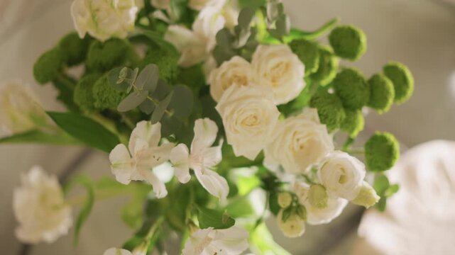 White rose bouquet on dining table, overhead view of lush roses and green button mums in vase, bright morning sunlight casting soft shadows, elegant home centerpiece for brunch or intimate