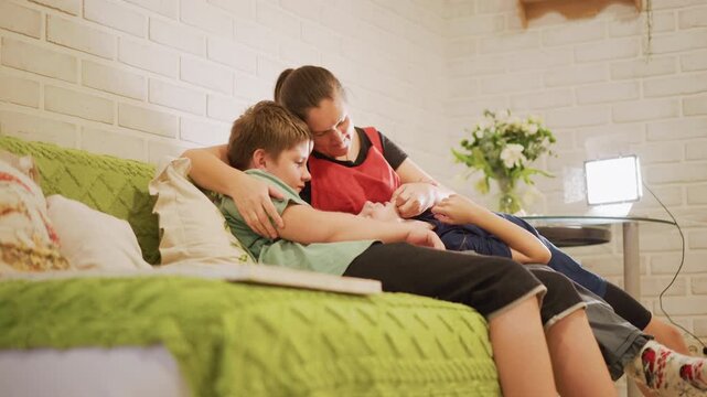 Caucasian mother and son laughing on sofa at home, playful evening unwind with tickles and smiles, green throw and bedside lamp create cozy mood, family relaxation and warm connection captured