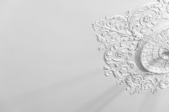 Ornate white plaster ceiling medallion with intricate floral molding and classical details set against a minimal white surface evoking vintage elegance, interior design and architectural craftsmanship