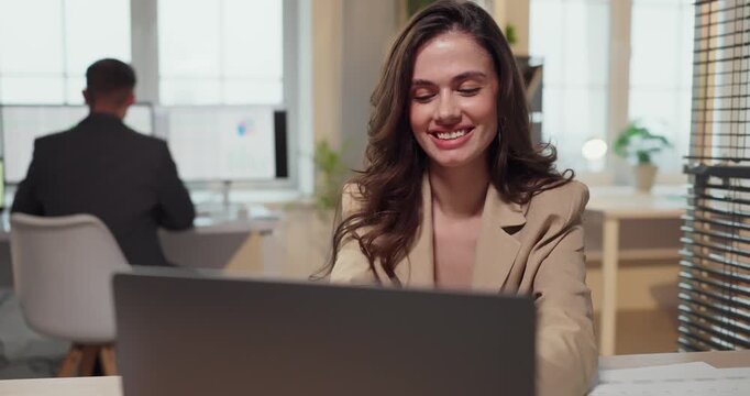 Woman happy about business success at laptop. She smiles with raised fists in an office, excited by achieved goals and strong performance metrics. Concept of achievement and career growth.