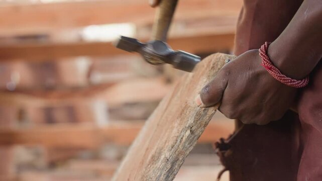 Closeup hands shaping wooden edge with chisel and mallet, dust particles flying in sunlit workshop, braided bracelet on wrist, steady carving motion creating smooth timber surface, traditional