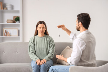 Obraz premium Young woman sitting on sofa during hypnosis session at psychologist's office