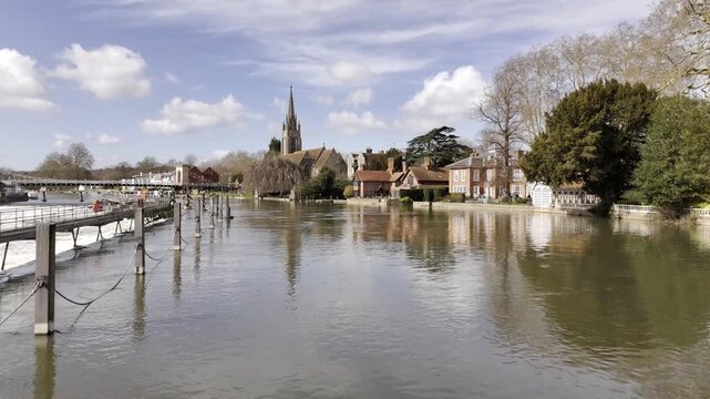 Smooth aerial drone footage flying past the church steeple of All Saints Church in Marlow, Buckinghamshire, before moving out over the River Thames. Scenic British riverside town with historic archite