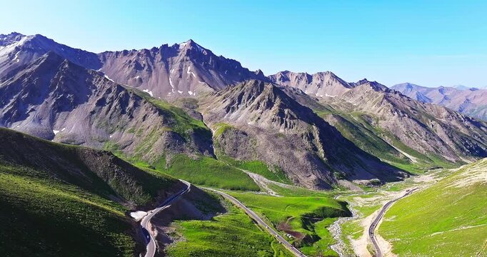 Aerial view of a winding serpentine road through a rugged mountain valley under clear blue sky, Xinjiang, China.