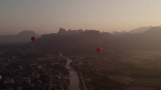 Vang Vieng, Laos - February 16, 2026: Hot air baloons flying around the city of Vang Vieng during late afternoon.