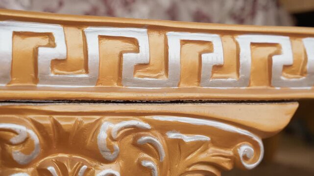 Closeup gilded wood molding shows intricate carved scrollwork, white highlights on gold paint, ornate profile and shallow depth of field, warm workshop lighting, restoration mood