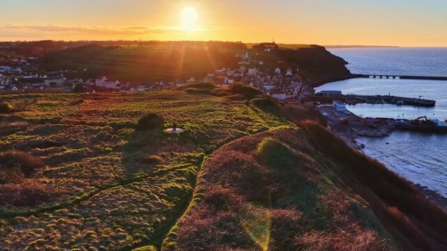 Drone flight over the coastline during an orange sunset to the village of Port-en-Bessin in France.
