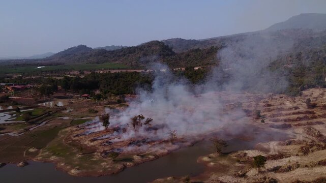 Aerial circling moving flying view of agricultural burning field during the slash and burn dry season in the countryside of Laos.