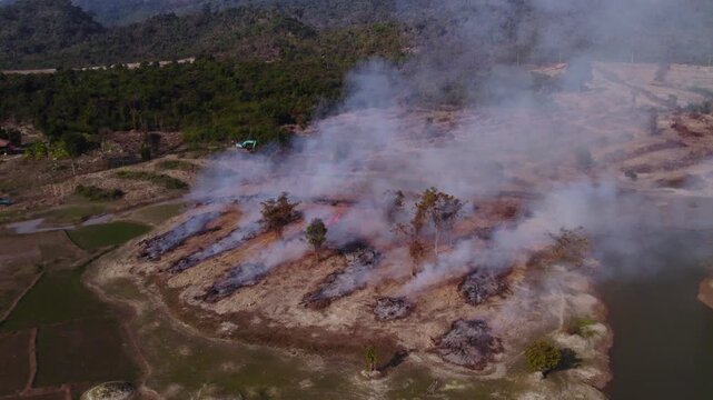 Aerial circling moving flying view of agricultural burning and demolition of field during the slash and burn dry season in the countryside of Laos.