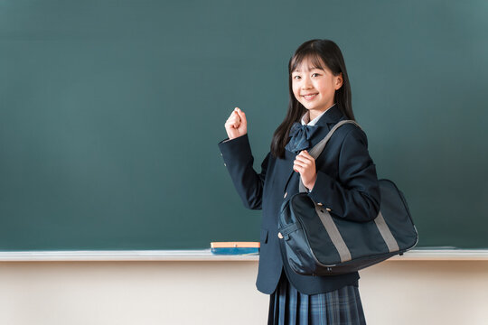 Female elementary, middle, and high school students in blazers stand in front of the blackboard and strike a triumphant pose.